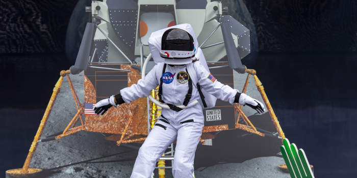 Ein als Astronaut verkleideter Darsteller steht vor einer Attrappe eines Raumschiffs auf dem Mond.