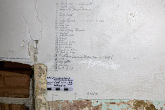 Teils aufgerissene Farbschicht einer Wand mit handschriftlichen Notizen