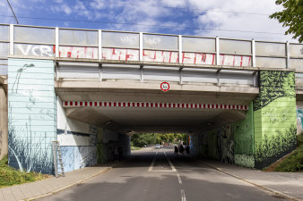 Eine Eisenbahnunterführung wird von vorn gezeigt, die Brückenpfeiler sind grün-blau bemalt.