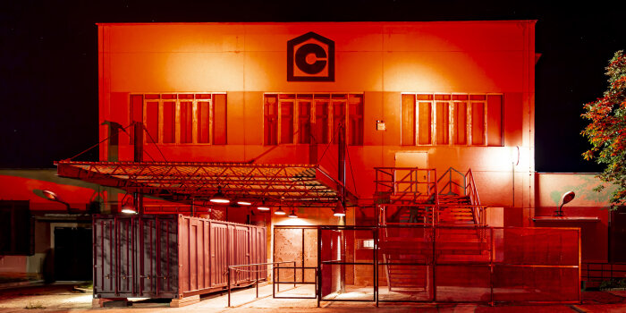 Ein Industriegebäude ist komplett rot angestrahlt, ein großes "C" steht auf dem Gebäude. Frontalaufnahme.