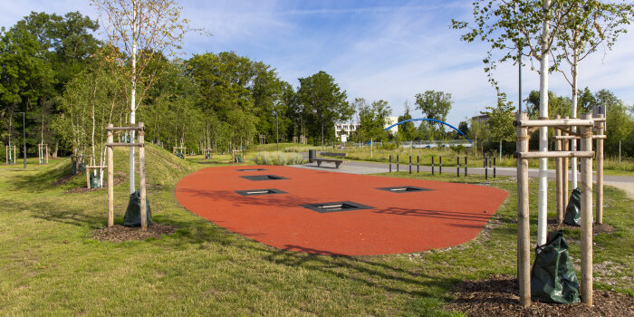 eine Trampolinlandschaft in einem Park, im Boden sind fünf rechteckige Trampoline eingelassen