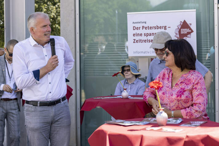 ein Mann spricht am Mikrofon, um ihn herum vier weitere Menschen
