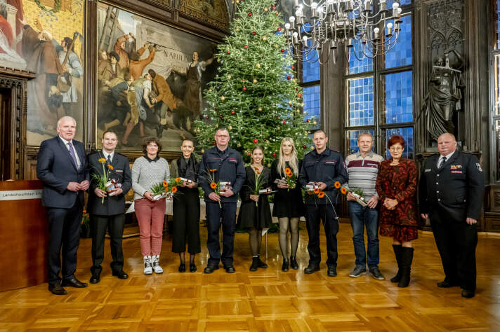 Eine Gruppe von Menschen steht vor einem Weihnachtsbaum zur Ehrenamtsfeier 2023. 