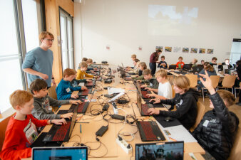 Mehrere Jugendliche sitzen an einem großen Tisch und arbeiten an Laptops