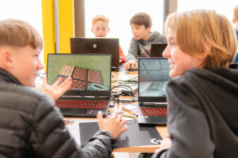 Zwei Jugendliche sitzen vor ihren Laptops und unterhalten sich