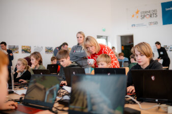 Zwei Frauen schauen Jugendlichen, die an einem Computer arbeiten, über die Schulter
