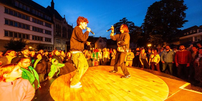 Musiker auf einer runden Bühne, um die Menschen stehen