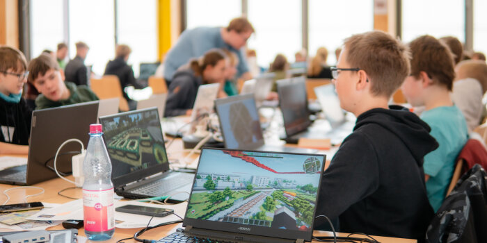 Mehrere Kinder sitzen an einem großen Tisch und arbeiten an Laptops