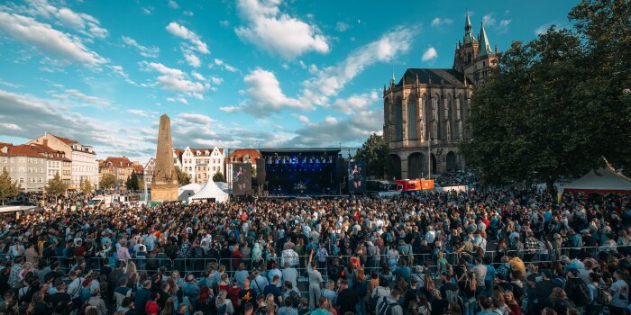 Viele Menschen vor einer Bühne, dahinter der Dom 