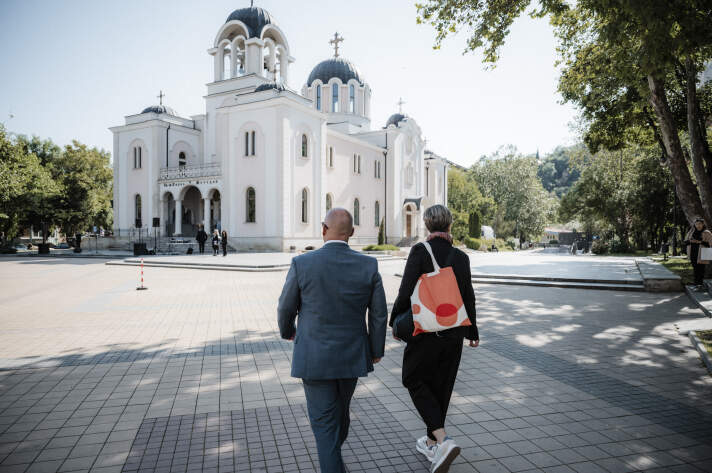 zwei Personen gehen auf ein weißes Kirchengebäude mit zwei runden Kuppeln zu
