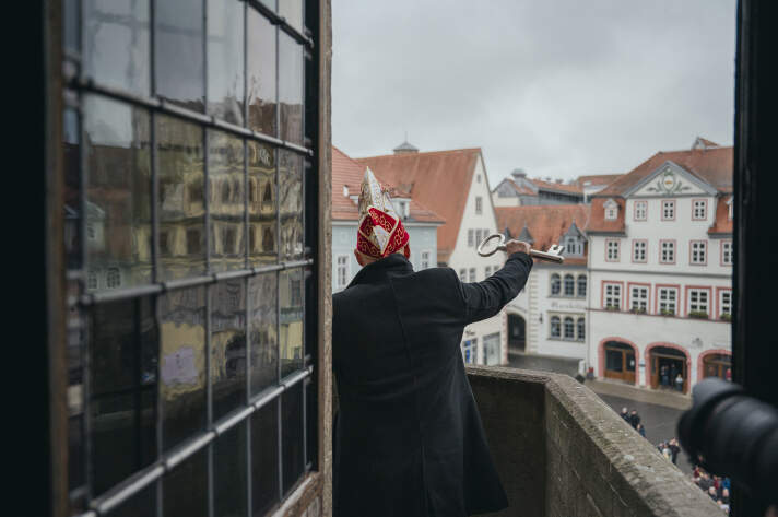 ein Mann mit Narrenkappe hält einen großen Schlüssel in die Höhe