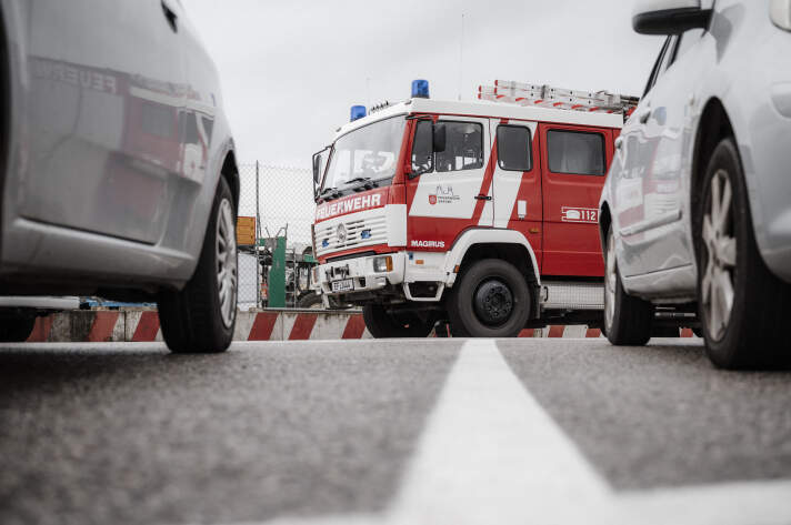 ein rot-weißes Feuerwehrfahrzeug steht zwischen anderen Fahrzeugen