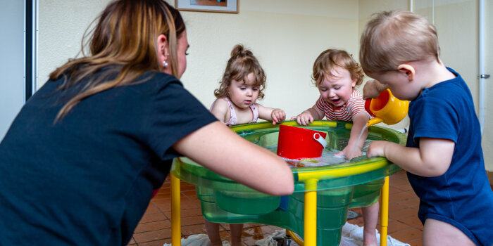 eine Frau und drei Kinder an einem Wasserbecken, die Kinder spielen mit dem Wasser