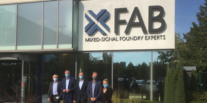 Vier Männer und eine Frau stehen vor einem Firmengebäude mit dem Logo „X-Fab“.