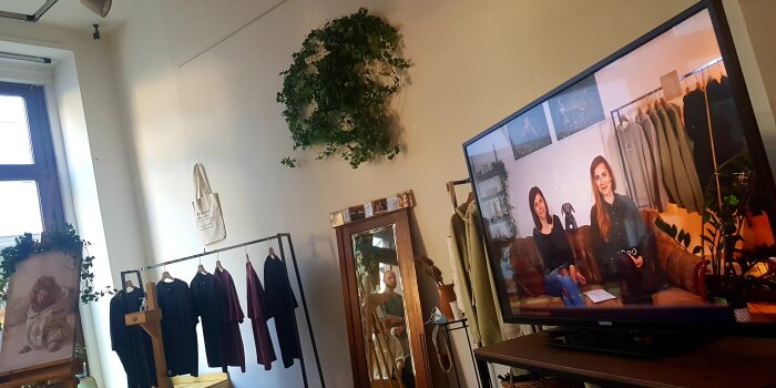 Foto: Pop-up-Store F11 - pawaho - Gründungsgeflüster - Film © Stadtverwaltung Erfurt Ein Ladenlokal mit Kleiderstange, auf der T-Shirts hängen und Bildschirm, auf dem zwei Frauen abgebildet sind.