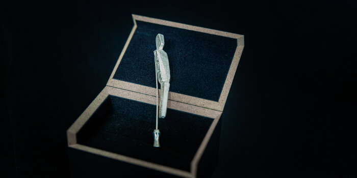 Foto: Ehrennadel Thüringer Engagement-Botschafter 2022 © Mario Hochhaus Ehrennadel in Form einer menschlichen Skulptur in einer Schatulle vor schwarzem Hintergrund