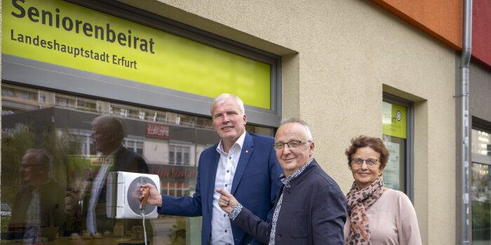 Zwei Männer und eine Frau testen einen Fensterputzer an einer Fensterscheibe.