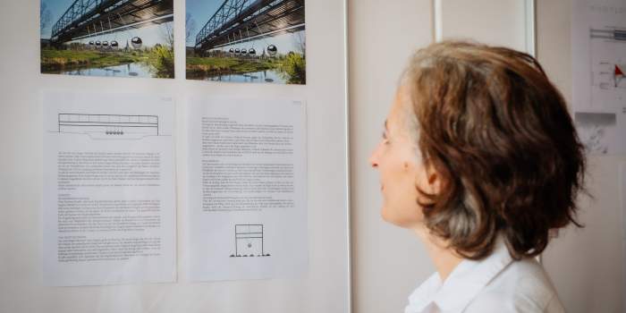 Eine Frau schaut auf eine Wand mit Enttwürfen von Brücken und dazugehörigen Text darunter.