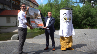 Zwei Männer halten Plakat aufgespannt; nebenan steht eine als lebensgroße Zigarette verkleidete Person