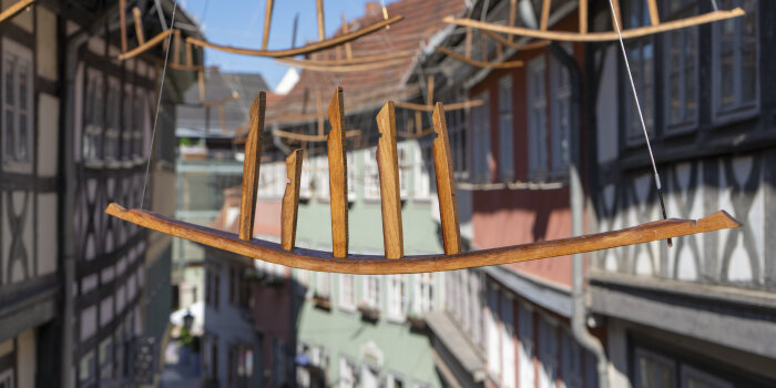 Kunstinstallation auf historischer Brücke; Holzskulpturen hängen an Seilen über Krämerbrücke