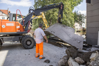 Zwei Bagger heben einen Streifen Beton nach oben, ein Bauarbeiter überwacht die Arbeiten.