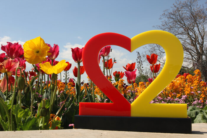 Das Logo zum Tag der Deutschen Einheit - eine herzförmige 22 - vor Tulpen, Mohn und anderen Blumen.