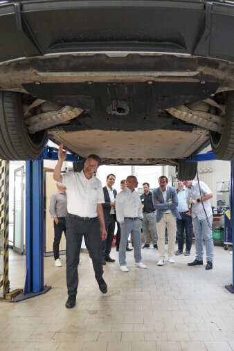 ein Mann steht erklärend unter dem Unterboden eines Autos, mehrere Männer stehen dahinter