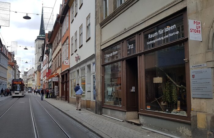 Ladengeschäft in einer Straße mit Passanten und Straßenbahn im Hintergrund