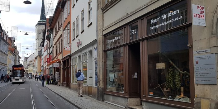 Ladengeschäft in einer Straße mit Passanten und Straßenbahn im Hintergrund