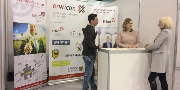 Foto: Ignition 2018 © Stadtverwaltung Erfurt Auf dem Foto ist ein Messestand d. Wirtschaftsförderung zu sehen, an dem 2 Berater stehen und eine Person beraten.