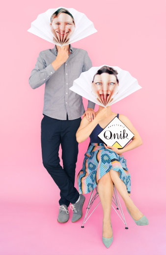 Zwei Menschen halten sich einen Fächer mit als Foto aufgedruckten Gesichtern vor den Kopf. 