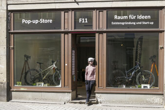 eine Person mit Fahrradhelm steht in der Tür eines Ladengeschäfts, in den Schaufenster sind Fahrräder