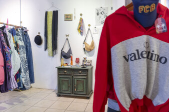 eine grüne Holzkommode steht zwischen Kleiderständern, an der Wand hängen Handtaschen und Schals