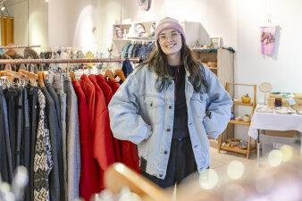 eine Frau in heller Jeansjacke steht zwischen Kleiderständern