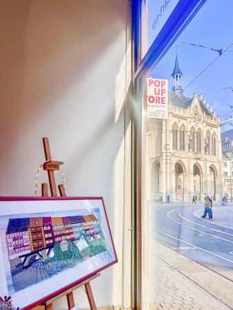 in einem Schaufenster steht ein Bilderrahmen mit einer geklöppelten Krämerbrücke