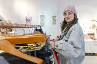 eine Frau in heller Jeansjacke steht an einem befüllten Kleiderständer