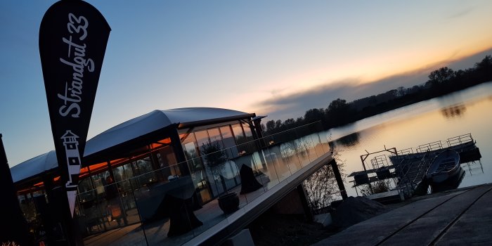 Strandbar mit Wasserzugang und Booten am Steg im Hintergrund