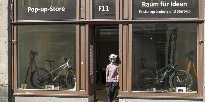 eine Person mit Fahrradhelm steht in der Tür eines Ladengeschäfts, in den Schaufenster sind Fahrräder