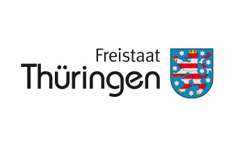 Das Logo zeigt rechts das Wappen Thüringens, einen rot-weiß gestreiften Löwen mit Krone auf blauem Grund, links daneben den Schriftzug "Freistaat Thüringen" in schwarzer Schrift auf weißem Grund.