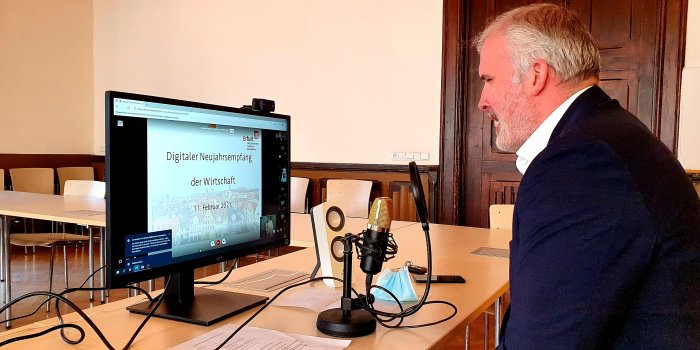 Erfurts Oberbürgermeister sitzt am Mikrofon vor einem Computerbildschirm