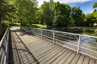 Holzbrücke vor Teich und Park, neben Straße des Friedens