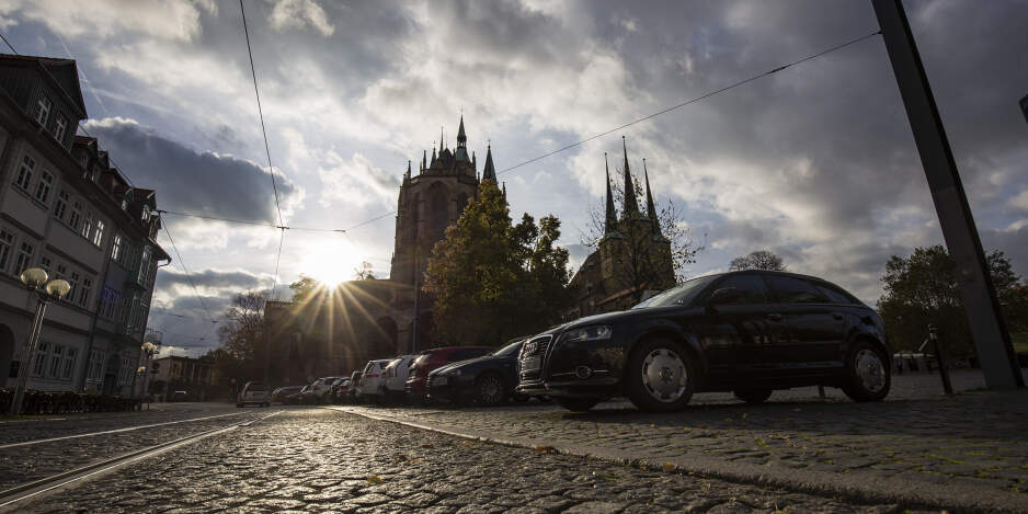 Straße mit Kopfsteinpflaster, parkende Autos, im Hintergrund der Dom