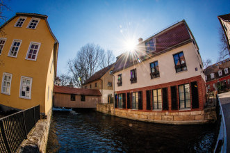 Blick über Fluss auf überdachte Holzbrücke