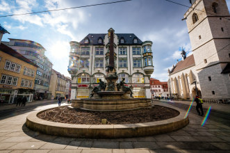 Blick auf Brunnen ohne Bepflanzung; rechts die Katholische Kirche Sankt Wigbert