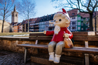 Sandmann-Skulptur sitzt auf Bank in Kreuzgasse