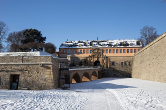 Blick auf die Zitadelle auf dem Petersberg von einer zugeschneiten Wiese aus. Zu sehen ist sowohl die Treppe, als auch die Brücke, die zu der Zitadelle führt.