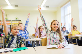 Schulkinder sitzen an ihren Bänken und melden sich motiviert.