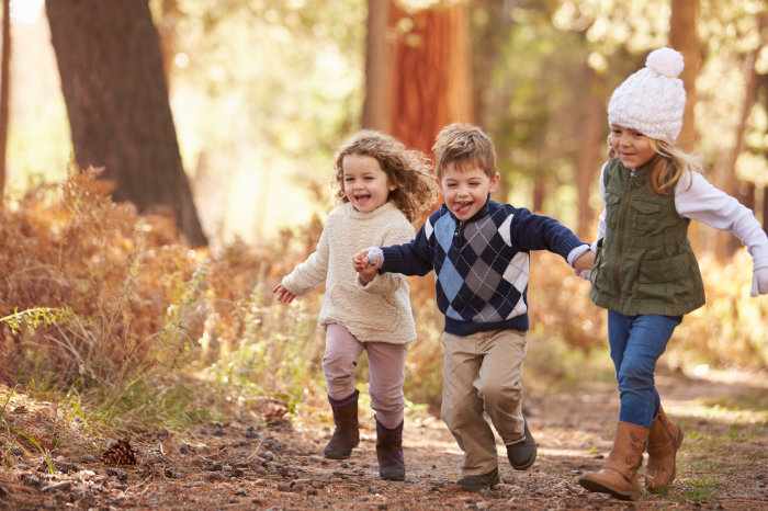 Drei kleine Kinder rennen lachend durch den Wald im Herbst.