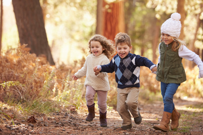 Spielen im Wald Drei kleine Kinder rennen lachend durch den Wald im Herbst.