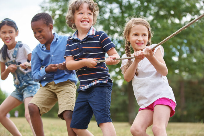 Vier Kinder ziehen, offensichtlich während eines Wettkampfes, draußen im Grünen gemeinsam an einem Seil.